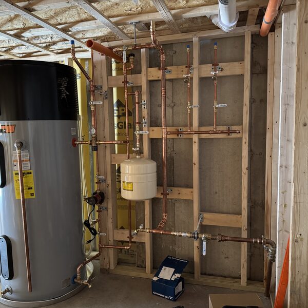 Hybrid heat pump water heater beside a new copper distribution manifold