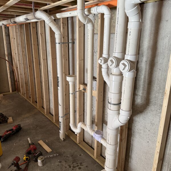 PVC waste and vent stack rough-in along a framed basement wall